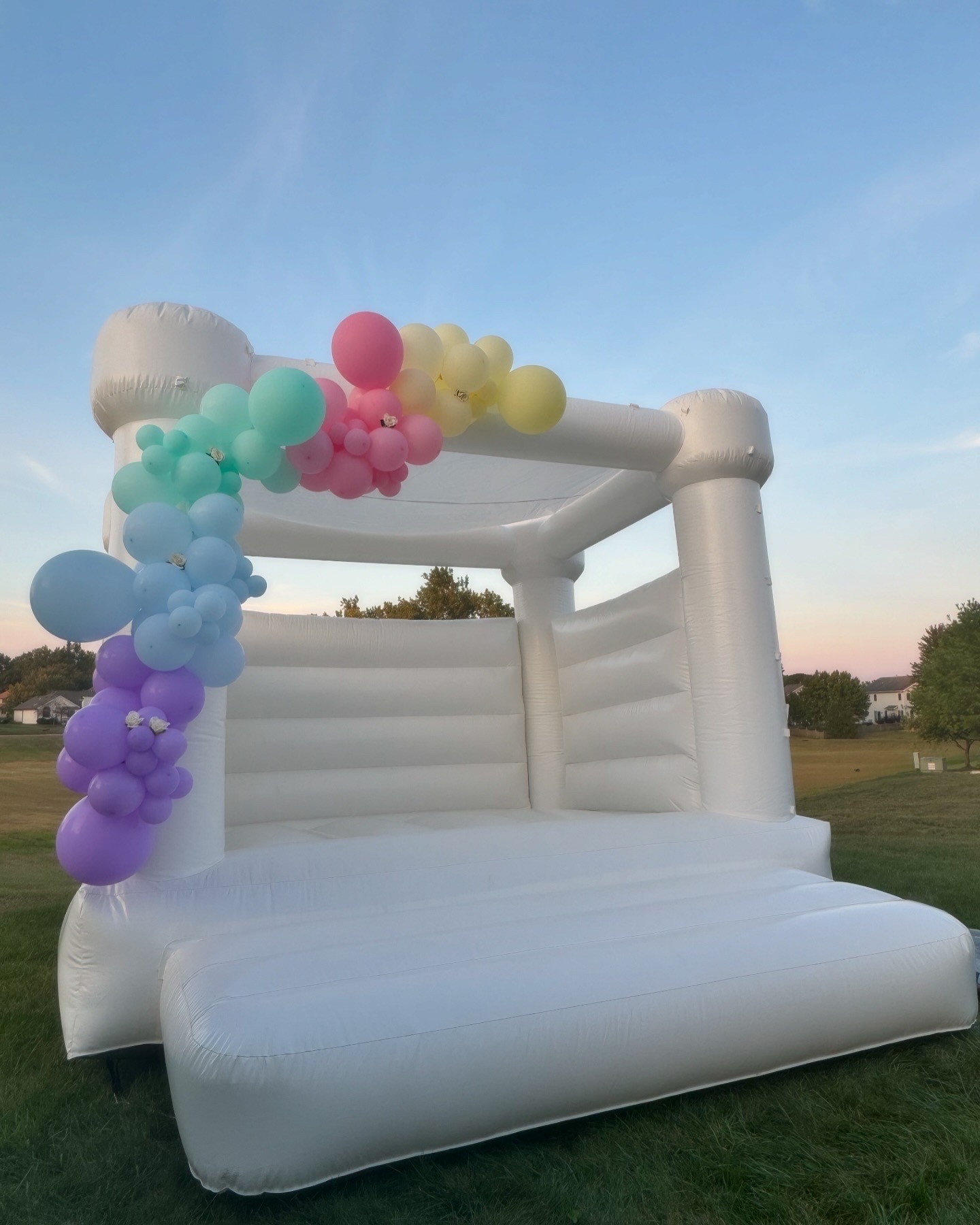 White bounce house rental in Fort Wayne Indiana with rainbow balloon garland at sunset